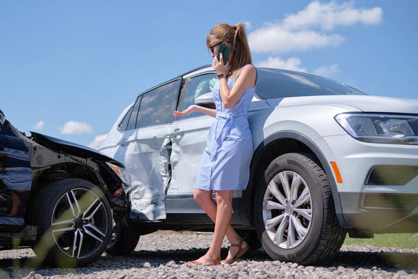 Stressed driver talking on sellphone on roadside near her smashed vehicle calling for emergency service help after car accident. Road safety and insurance concept. - Photo, Image