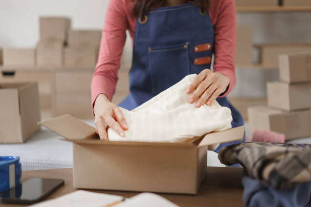 Концепция онлайн-шопинга, женщины-предприниматели упаковывают одежду в коробку для доставки клиенту. - Фото, изображение