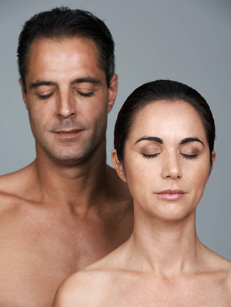 At peace with their bodies. Studio shot of a mature couple with their eyes shut standing together against a gray background - Foto, Imagem