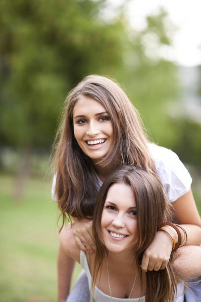 Lovely and lively and enjoying life. a young woman giving her friend a piggyback ride at the park - Photo, image
