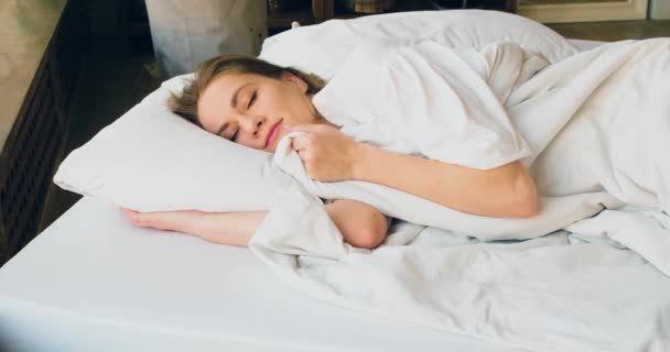 4K beelden van een vrouw slaapt, ze maakt de deken recht, glimlacht in haar slaap en ligt comfortabeler. Close-upzicht. - Video