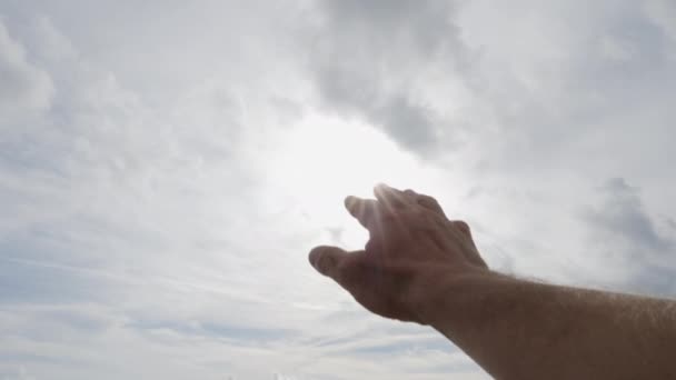 Mans hand palm reaching toward the sunshine into a cloudy sky - Filmati, video