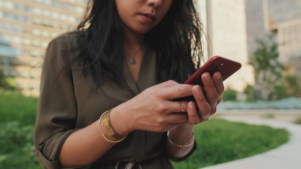Close-up, Young girl uses smartphone while sitting on modern buildings background - Photo, image
