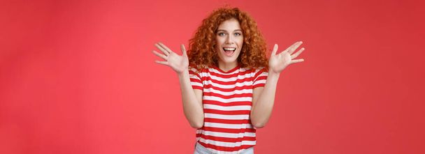 Awesome incredible performance bravo. Attractive cheerful cute european redhead curly female raise hands thrilled express excitement happiness joy look camera entertained delighted red background. - Photo, Image