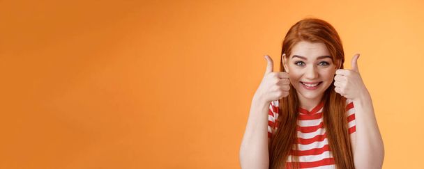 Hopeful cheerful cute redhead girlfriend rooting for you, believe win, smiling supportive satisfied, show thumbs-up delighted, approve choice, wish good luck, encourage friend, orange background. - Photo, Image