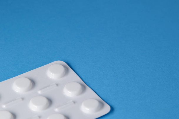 Blauwe achtergrond met een pakket van medische pillen op de rand van het beeld. Blauwe medische achtergrond met vrije ruimte voor tekst, kopieerruimte - Foto, afbeelding