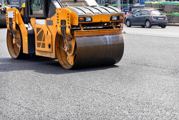 A vibrating roller rams and compacts fresh asphalt on a city street on a summer day among the roadway. Close-up. Copy space. - Zdjęcie, obraz