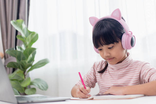 Ασιατικό κοριτσάκι στα ακουστικά έχουν βίντεο κλήση μακρινή τάξη με δάσκαλο χρησιμοποιώντας φορητό υπολογιστή, μελέτη σε απευθείας σύνδεση στον υπολογιστή, κατ 'οίκον διδασκαλία έννοια - Φωτογραφία, εικόνα