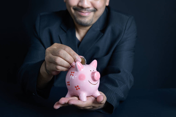 businessman putting money coin into piggy for saving money wealth and financial concept. - Photo, Image