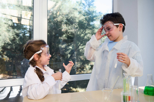 Adorable Caucasian diverse kids enjoying chemistry lesson in a school laboratory. School Children wearing white lab coats and safety goggles, conducting chemical experiments. Back to school concept - Foto, immagini