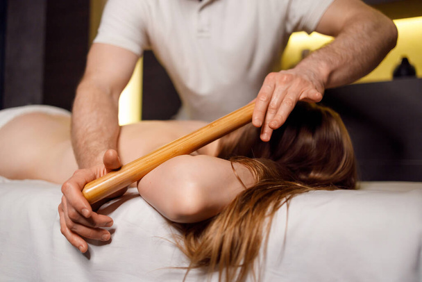 Woman is getting massage with bamboo stick in spa - Foto, afbeelding