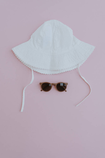 夏のベビーアクセサリー。パステルピンクの背景にパナマの帽子とサングラス。フラットレイアウト、トップビューミニマリストベビーファッションセット - 写真・画像