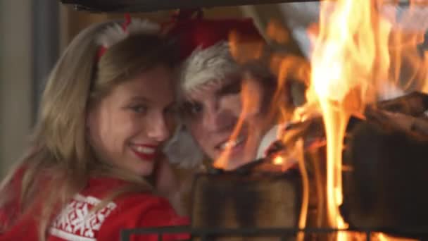 CLOSE UP: Burning fire flames and cute romantic couple leaning on each other. View of fireplace and young twosome in love enjoying romantic atmosphere in home living room on festive winter Evening. - Filmati, video