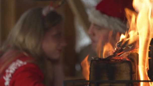 CLOSE UP: Burning flames and cute couple sharing romantic moments on Christmas. View of fireplace and young twosome in love enjoying cosy atmosphere in home living room on festive winter Evening. - Séquence, vidéo