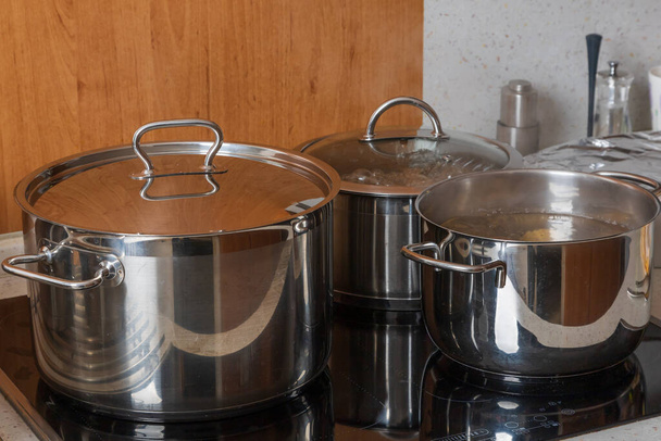 Metal silver pots on the stove in the kitchen. Glass ceramic cooking plate. - Foto, imagen