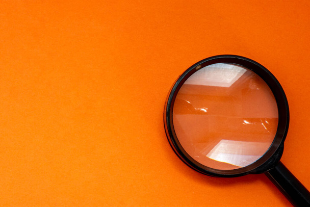 Black magnifying glass for reading or as a tool of investigation is on a orange background with a clean half photo region for labels or headers. Illustrative photo for orange designs - Foto, afbeelding