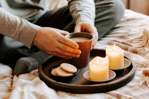 een blanke man die thuis ontspant, kaarsen aansteekt, koffie drinkt in bed onder de deken - Foto, afbeelding