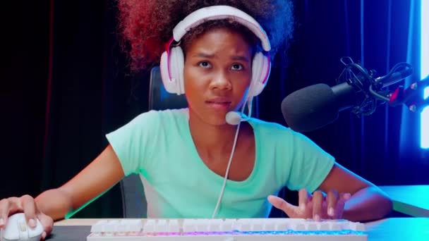 Νεαρή Αφρο-Αμερικανίδα που φοράει ακουστικά και παίζει βιντεοπαιχνίδι και ζει σε απευθείας σύνδεση με μικρόφωνο στο σπίτι, gaming και esport για ανταγωνισμό ή χύτευση παιχνιδιών, μετάδοση και ψυχαγωγία έννοια. - Πλάνα, βίντεο