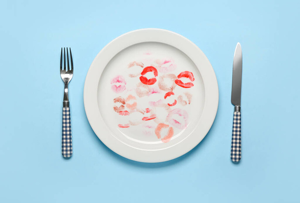 Plate with lipstick kiss marks and cutlery on blue background - Zdjęcie, obraz