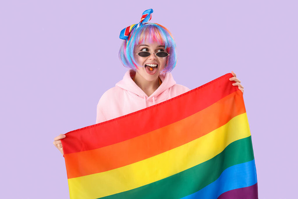 Beautiful young woman with candy and LGBT flag on lilac background - Zdjęcie, obraz