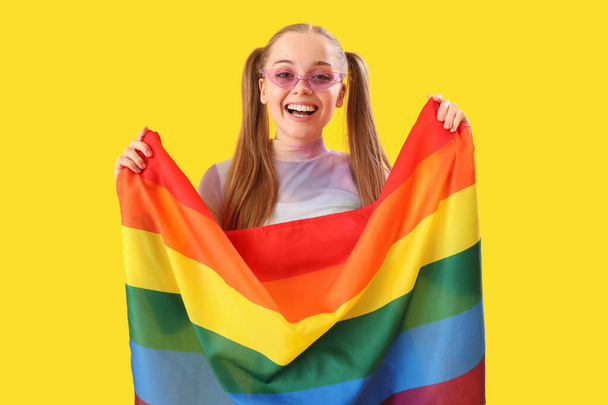 Beautiful young woman in sunglasses with LGBT flag on yellow background - Foto, Bild