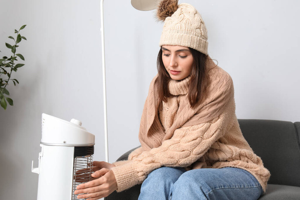 Frozen young woman warming near electric heater at home - Foto, imagen