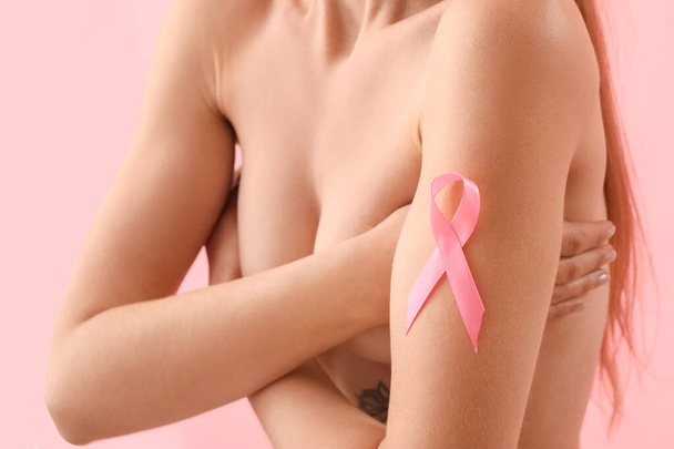 色の背景にピンクのリボンを持つ裸の若い女性、クローズアップ。乳がんの認知概念 - 写真・画像