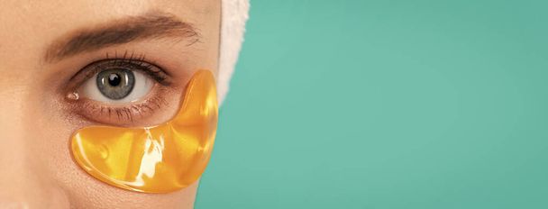 closeup of young lady has collagen golden eye patches on face with towel. Beautiful woman isolated face portrait, banner with mock up copy space - 写真・画像