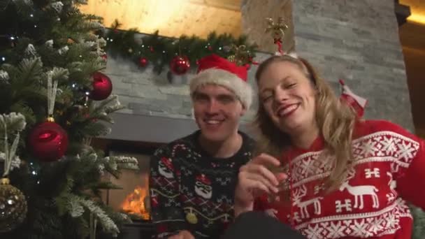 PORTRAIT:かわいい陽気なカップルがクリスマスツリーで一緒に踊り、歌います。笑顔男と女でお祝いのドレス気分で幸せなクリスマスのお祝い中とカメラにキスを吹いて. - 映像、動画