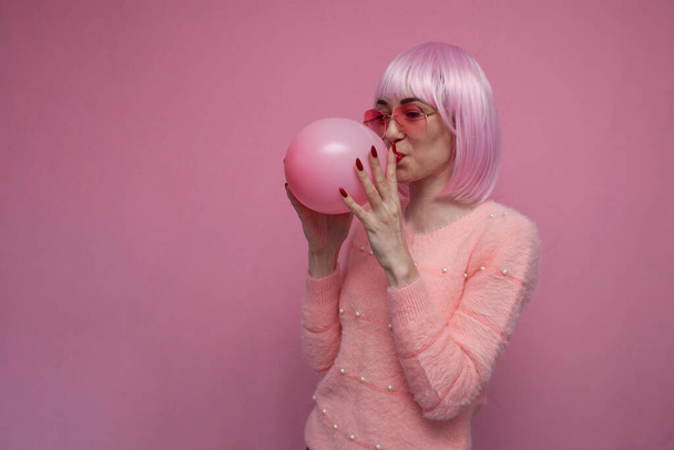 young girl with pink hair inflates a pink balloon on a pink background - Photo, image