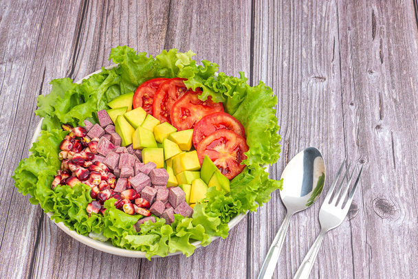 Green lettuce salad with fresh mixed purple corn, purple yams, avocado, and tomatoes on wooden table background. Space for text. Concept of healthy foods and vegetables. - Photo, Image