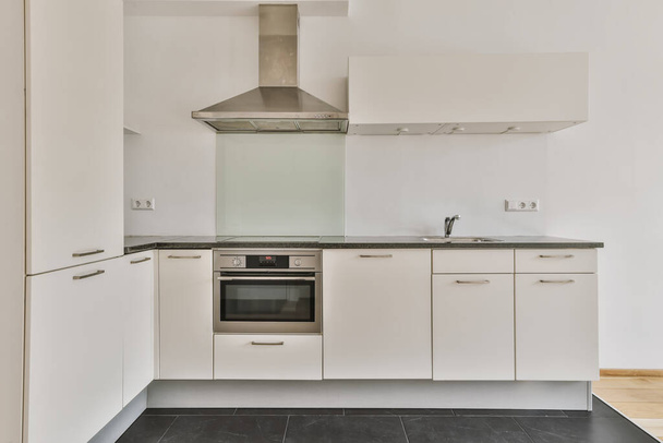 keittiö, jossa on valkoiset kaapit ja mustat työtasot lattialla uunin edessä, pesuallas ja astianpesukone - Valokuva, kuva