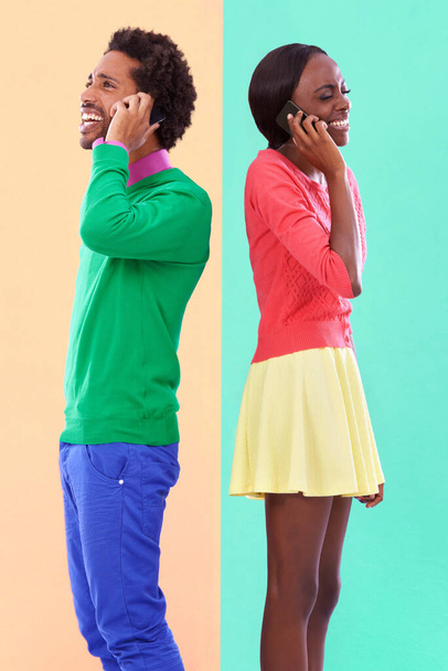 Hipster convo. Studio shot of a young couple using cellphoes standing against a colourful background - Foto, Imagen