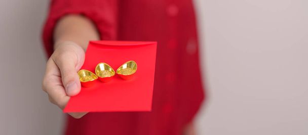 Woman holding Chinese red envelope with gold bullion, money gift for happy Lunar New Year holiday. Chinese sentence means happiness, healthy, Lucky and Wealthy - Photo, image