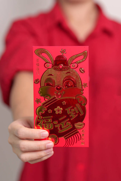 woman holding Chinese red envelope with golden rabbit and blessing word, money gift for happy Lunar New Year holiday. Chinese sentence means happiness, healthy, Lucky and Wealthy - Zdjęcie, obraz
