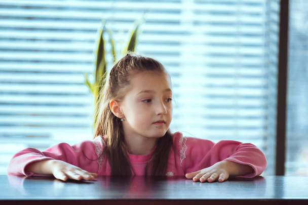 Child sitting on the table looking away to side. Portarit of a little girl in deep thought. download image - Foto, Bild