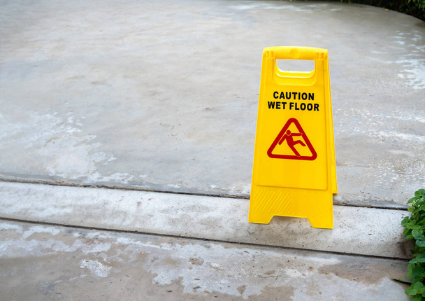 コピースペースで雨が降った後、濡れたコンクリート床の背景に滑りやすい人警告アイコンと黄色の注意滑りやすい濡れた床の看板. - 写真・画像
