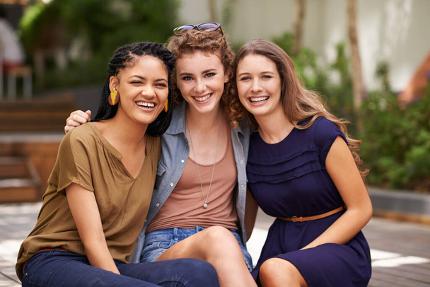 Дружба це не велика річ, її мільйон дрібниць. Портрет трьох молодих друзів, які посміхаються щасливо, сидячи на відкритому повітрі
 - Фото, зображення