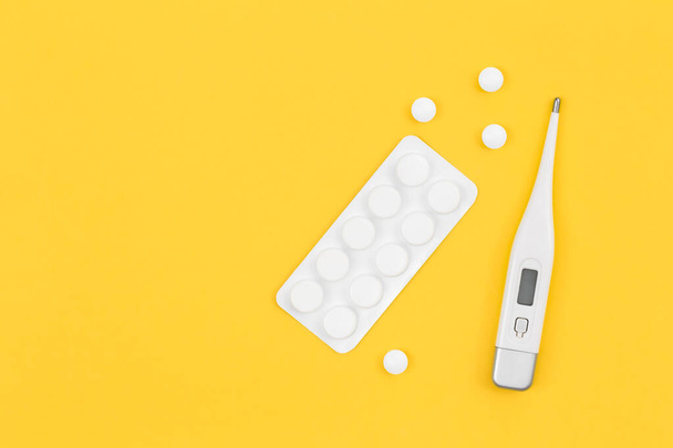 Pills and electronic thermometer on a yellow background, flat lay, copy space. - Foto, afbeelding