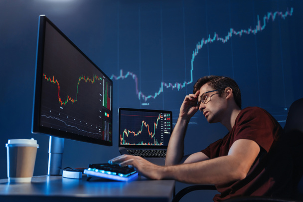 Crypto trader investor looking at computer screen with candlestick chart late night, thinking about global risks of online stock exchange market, upset with global recession and loss of money - Photo, image