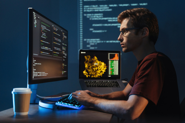 Προβολή προφίλ πορτρέτο του νεαρού επιστήμονα δεδομένων που εργάζονται στον υπολογιστή στο σπίτι αργά το βράδυ, αποσφαλμάτωση σενάριο κυβερνοχώρο σφάλμα, απομονώνονται στον τοίχο με zoomed ψηφιακή σελίδα - Φωτογραφία, εικόνα