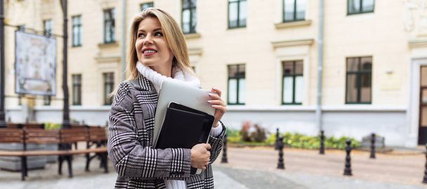 femme d'affaires blonde avec un ordinateur portable dans ses mains sur le fond de la ville. - Photo, image