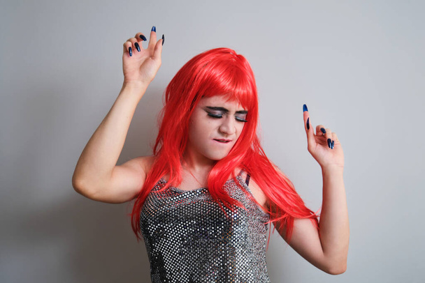 Porträt einer Drag Queen mit roter Perücke und Tanz auf grauem Hintergrund. LGBTQ queer. - Foto, Bild