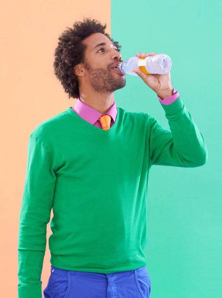 Mmmm...thats good. a stylish young man drinking from a bottle against a colorful background - Foto, Bild