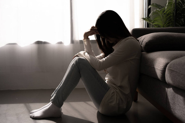 Молодая женщина чувствует себя подавленной и напряженной сидя в темной спальне. Концепция психического здоровья. - Фото, изображение