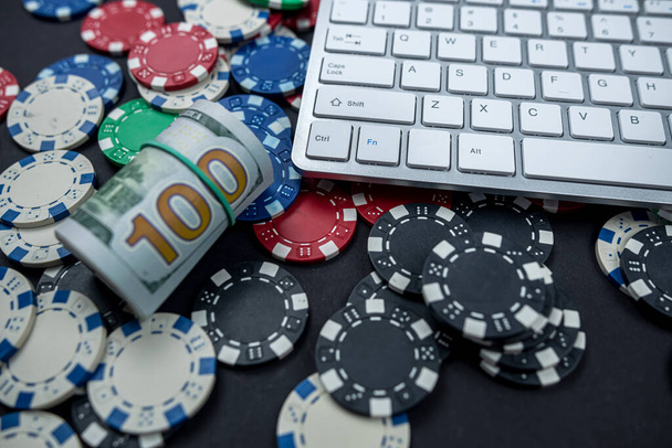 Poker żetony i paczki dolarów na klawiaturze laptopa rozrzucone na zwykłym tle. Hazard. nielegalne gry poker - Zdjęcie, obraz