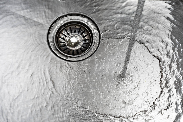 Running water drains down a stainless steel sink - Foto, imagen