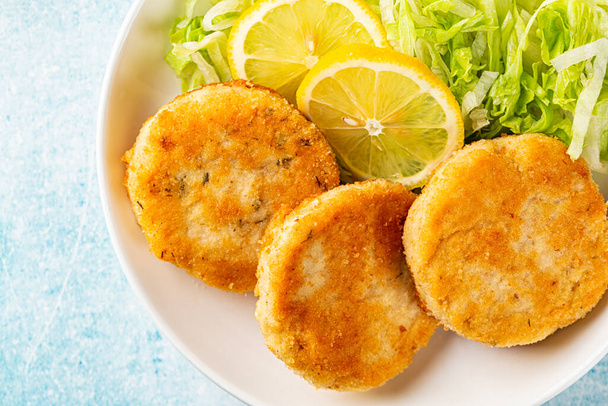 Top view of Fish cakes or burger, or cutlets. Made from ground perch and tuna with herbs, breaded and fried, served with iceberg salad, lemon slices. - Zdjęcie, obraz