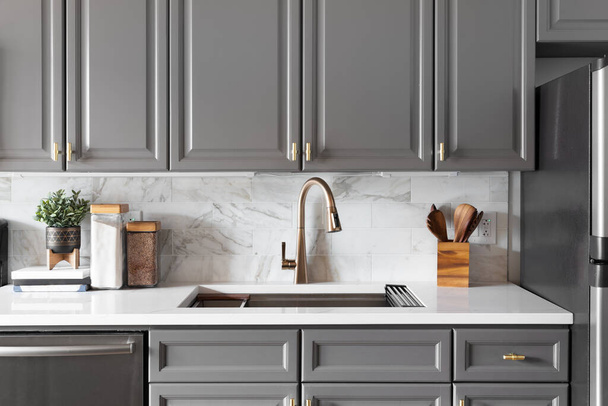 A kitchen sink detail shot with grey cabinets, a marble subway tile backsplash, and gold hardware and faucet. - Foto, afbeelding