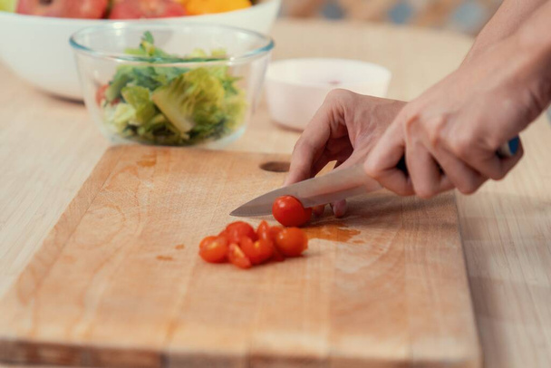 Close up hands holding a knife preparing a contented meal. Sliced tomatoes and other vegetables on the glass dish. - 写真・画像